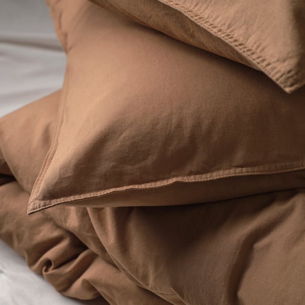 Close-up of soft, brown bed sheets stacked neatly on a bed, showcasing smooth fabric and stitching details.