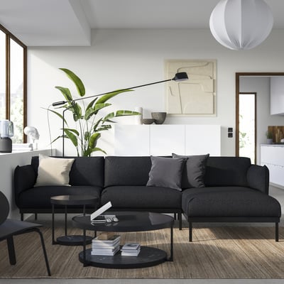 Modern living room with grey ÄPPLARYD sofa, pillows, black tables, plant, art, pendant lamp, wooden floor.