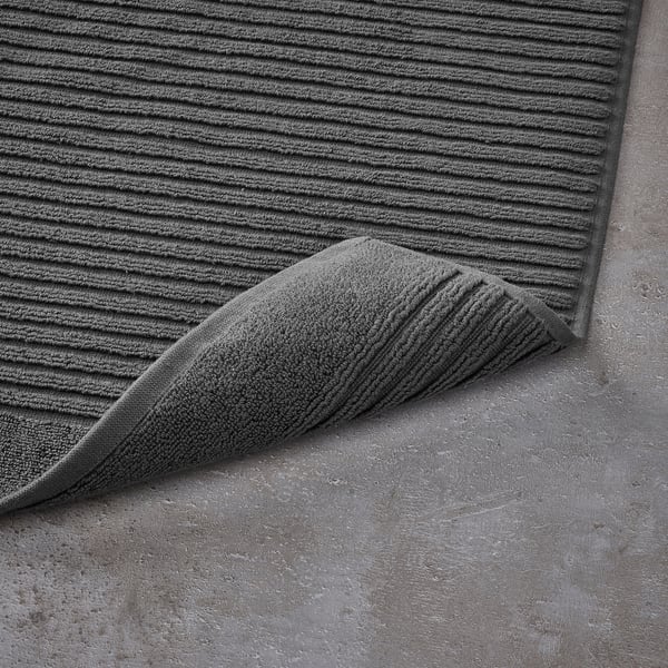 Dark grey textured bath mat with folded corner on grey stone floor.