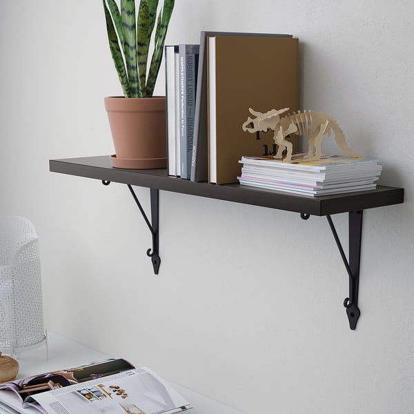 Wall-mounted shelf with black metal brackets holding books, magazines, a potted plant, and decorative items.