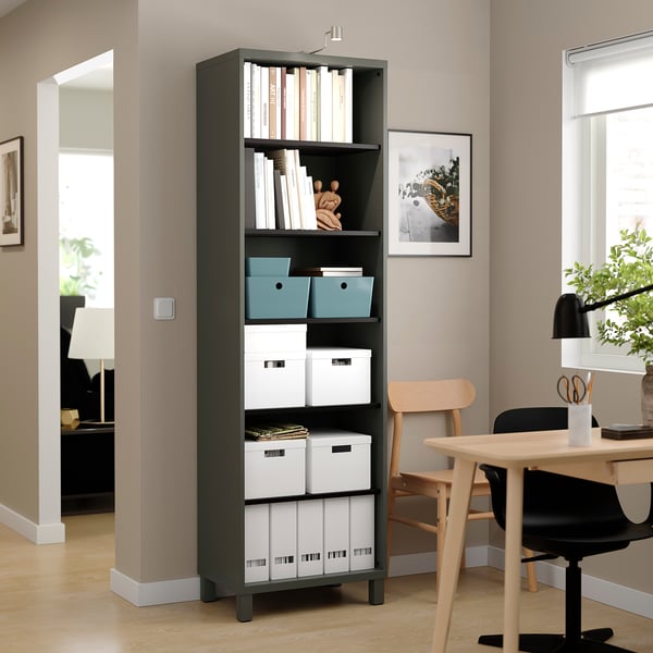 Black BESTÅ bookshelf with storage boxes and books, organised with decorative items, placed in a bright room with a chair nearby.