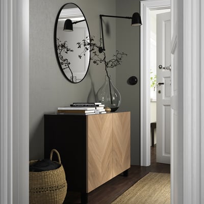 Minimalist entryway with BESTÅ sideboard, books, vase, basket, mirror, sconce.