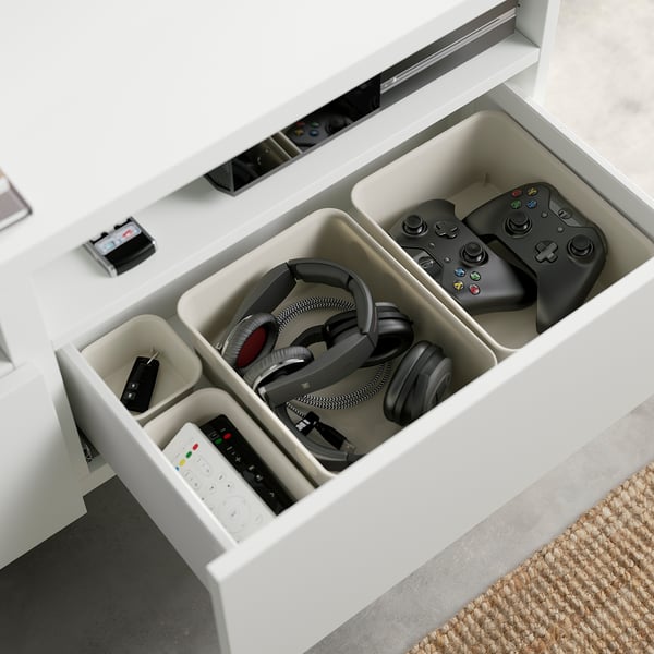 Open BESTÅ tv bench with organised gaming accessories: remote, headphones, controllers, and charging station.
