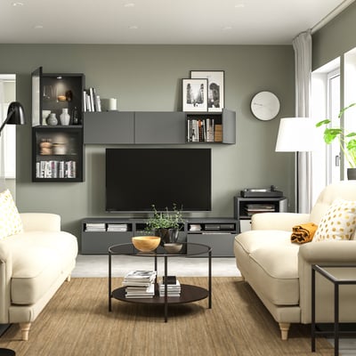 Modern living room with sage green walls, white couch, armchair, and flat-screen tv.