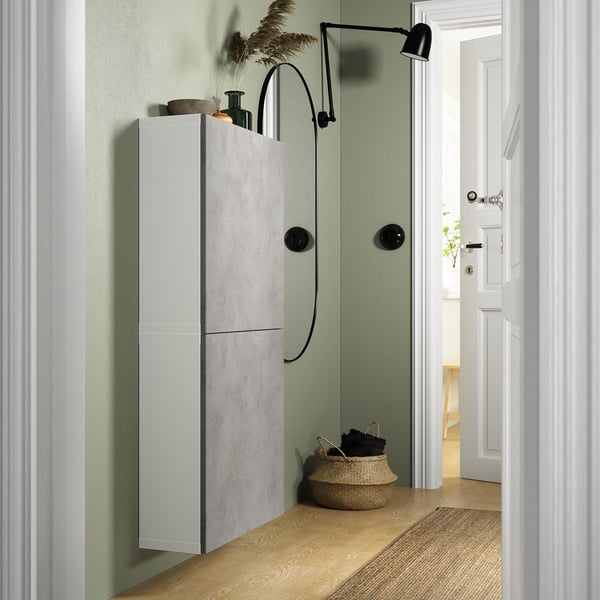 Narrow BESTÅ unit with 2 doors on green wall, white doors, black lamp, basket with towels.