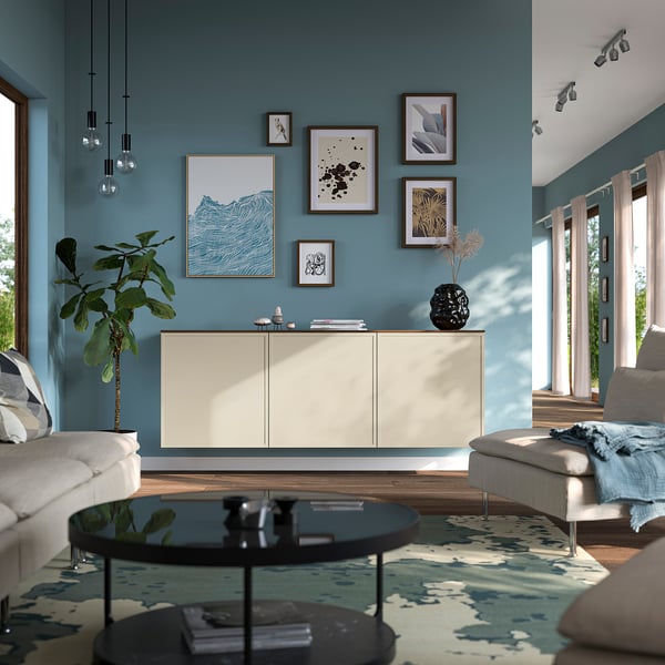 Modern living room with teal walls, white BESTÅ sideboard, glass coffee table, grey sofa, and patterned rug. Artwork displayed above sideboard.