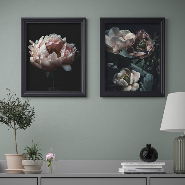 Two framed floral art prints hang above a console table displaying a lamp, vase, and plant.