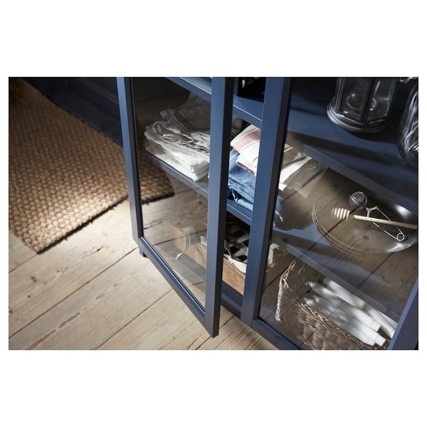 Blue mirrored cabinet with glass shelves storing towels and kitchen items.
