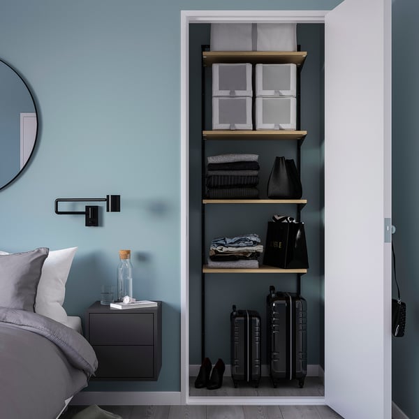 BOAXEL closet with black frames and wooden shelves, organised clothing, and bed with grey bedding and black side table.