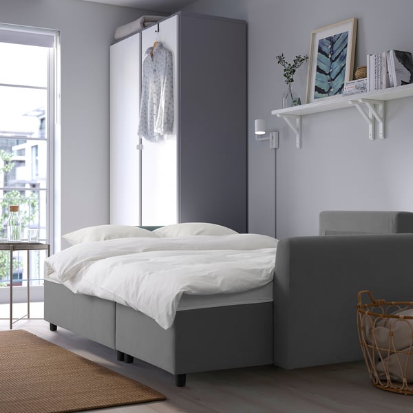 Modern compact living space with grey sofa bed, built-in storage, decor, and large window.