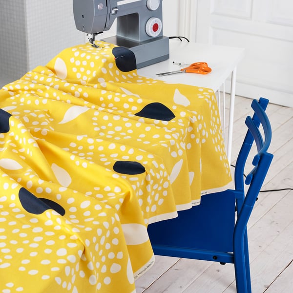 Bright yellow fabric with white flowers draped on a blue chair near a sewing machine.