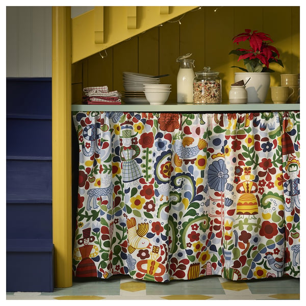 Bright kitchen with colourful floral curtain CINTIAKAKTUS, yellow walls, blue door, white dishes, red plant, and green floor.