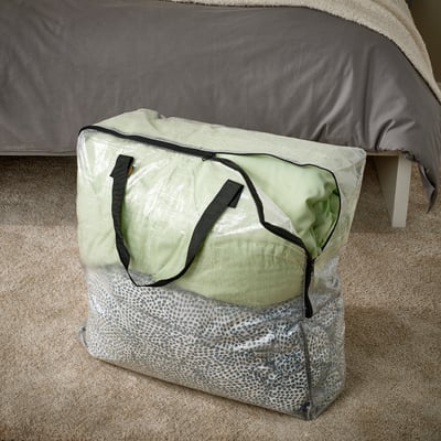 Clear plastic storage bag with handles, rests on beige carpet under bed.