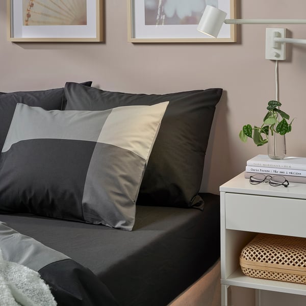 Black bed sheet with grey trim, patterned pillow, bedside table with items.