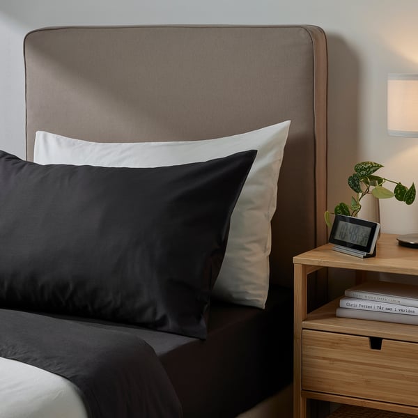 Bed with DVALA grey headboard, black pillows, nightstand, plant, and clock.