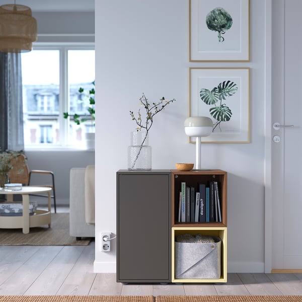 Modern living room with grey EKET storage. Books, fabric bin, closed cabinet. White lamp, vase, plant art.