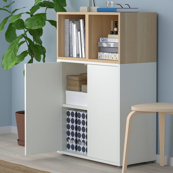 Wooden and white storage unit with open shelves and closed cabinets. It holds books, boxes, and a plant.