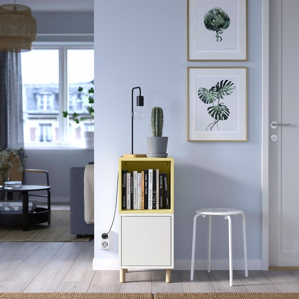 Modern living room with blue walls, EKET unit, cactus, and art prints. White stool nearby.