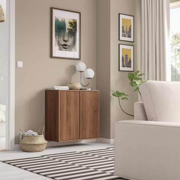 Modern room with wooden EKET cabinet, black-white rug, and grey armchair. Art and plants decorate the space.
