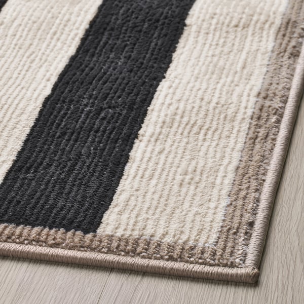 Striped rug with thick, soft texture; black, white, beige colours; high-quality materials.