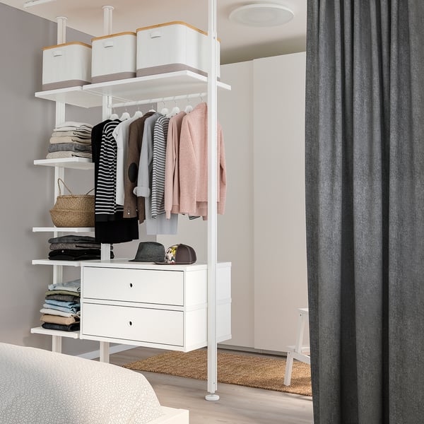 White ELVARLI wardrobe with clothes, drawers, shelves, and grey curtain in tidy bedroom.