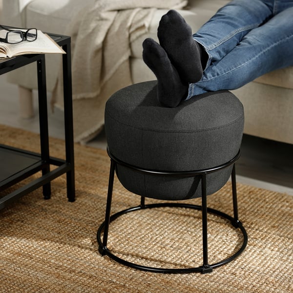 A person relaxes on a sofa with feet up on an EMMISLÖV pouffe, showcasing its use as a footrest.