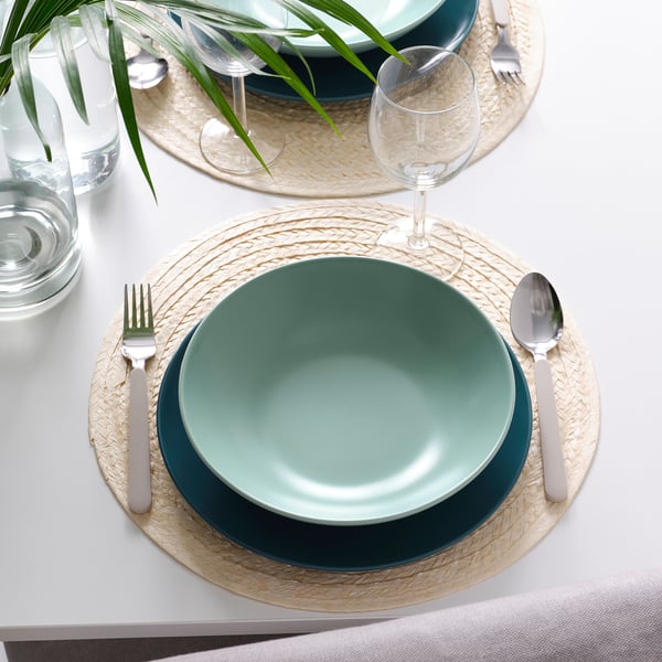 Table setting with FÄRGKLAR deep green plates, natural placemats, silverware, and glasses.