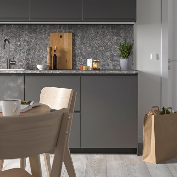 Modern grey kitchen with marble, wooden chairs, sleek fridge, and marble counter with cutting board and items.