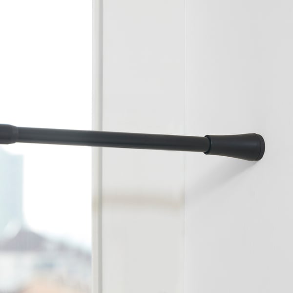 Black adjustable curtain rod mounted on a white wall, extending from 70 to 120 cm, featuring rubber caps at ends to prevent scratches.