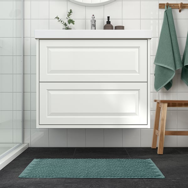 A bathroom with a white cabinet and sink, green bath mat, towels, and plants.