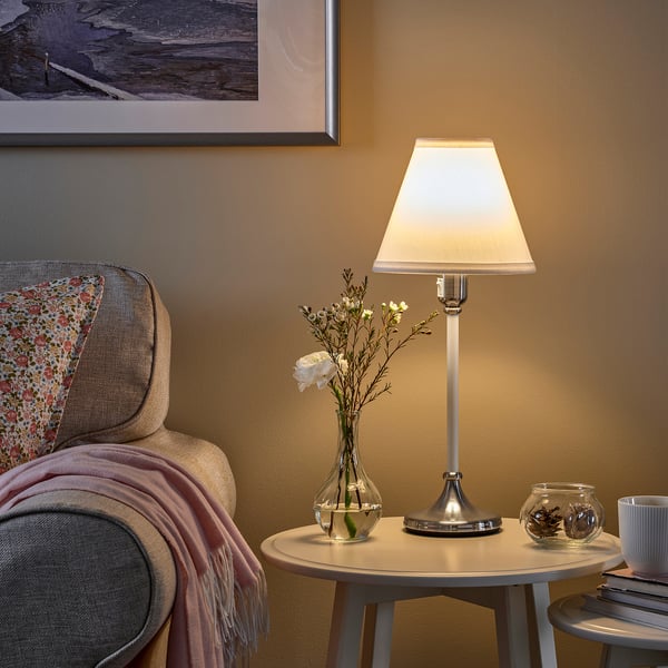 Cosy corner: lamp, armchair, flowers, books, warm light.