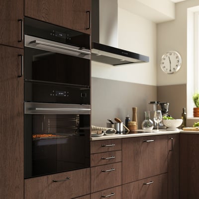 Modern kitchen with FRILLESBO stainless steel oven, digital controls, dark wood cabinets, and wall clock.