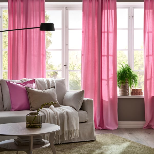 Pink curtains frame large windows, adding colour and privacy. Neutral armchair with pillows completes cosy, inviting space.