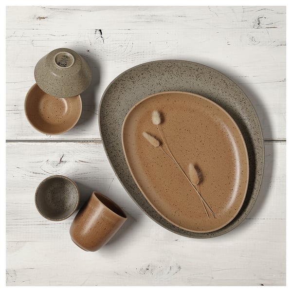 Rustic stoneware table set in brown on white wood, includes bowls, cups, plate with speckled design and dried grass decor.