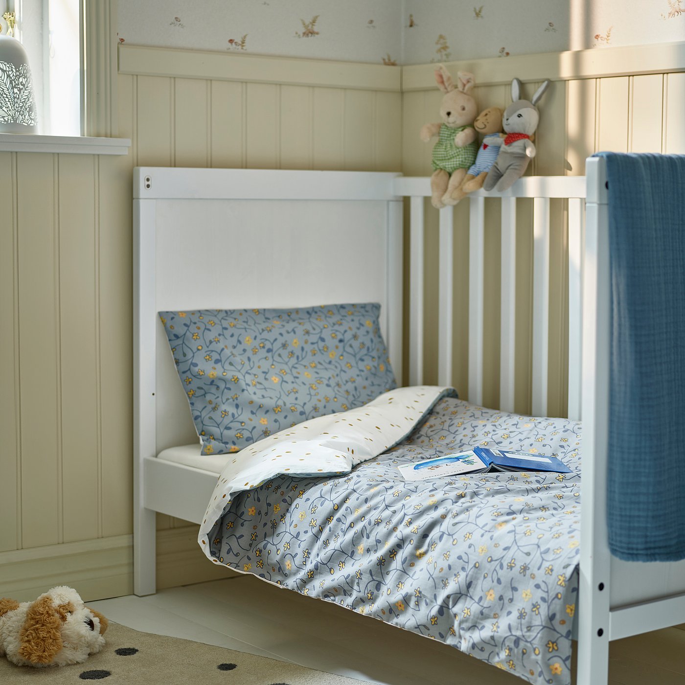 Kids bed under window, blue floral duvet, stuffed animals.