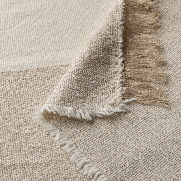 Lightweight, soft beige throw with intricate weave and fringed edges, made from recycled polyester.