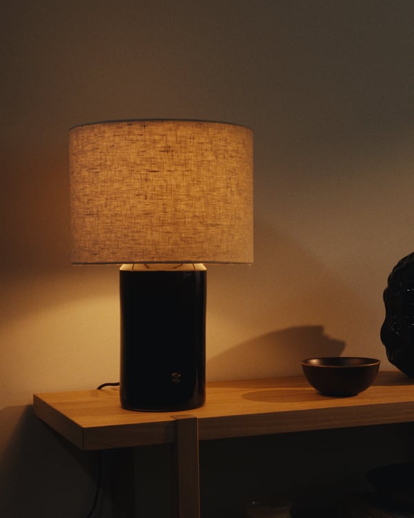 A modern lamp, HALGATT, in dark blue with a linen shade on a wooden shelf, emitting warm light.