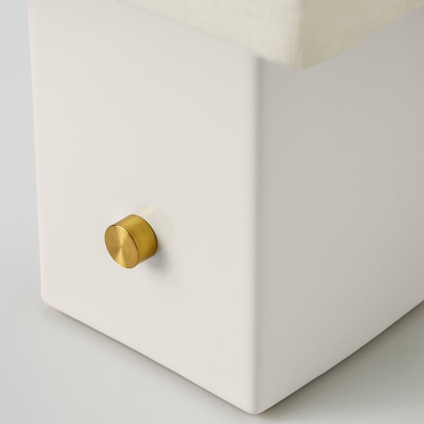 A sleek, modern lamp base with a golden knob on a smooth white surface.