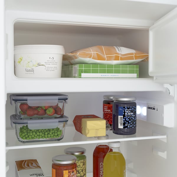 Fridge shelf with adjustable glass shelves, holding strawberries, peas, cheese, and jars. Led light on.