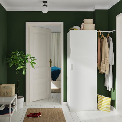 Green room with white organiser, clothes rail, baskets, hooks, natural materials, white door, plant.