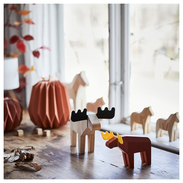 HÖSTAGILLE moose decor. Small wooden moose, brown with yellow antlers, standing near larger orange pumpkin and wooden horses.