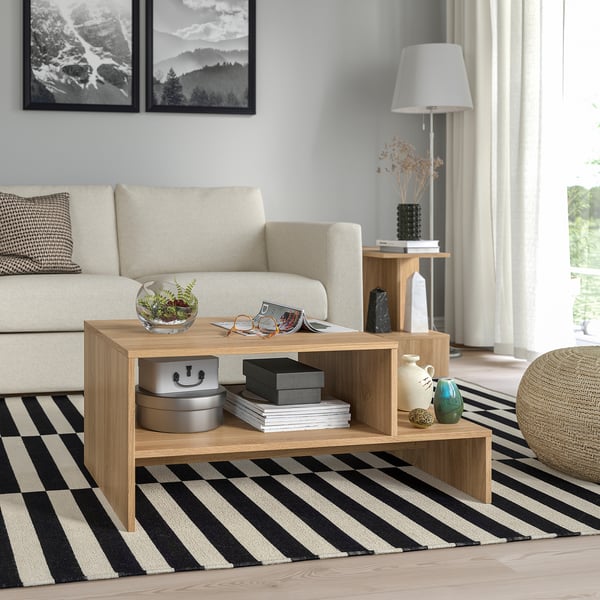 Modern living room with HOLMERUD light wood coffee table, cushioned beige sofa, black & white striped rug, and decorative items.