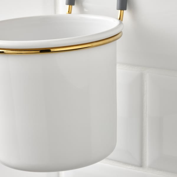 A hanging kitchen bowl, white with a gold ring, attached to a grey hook on a rail.