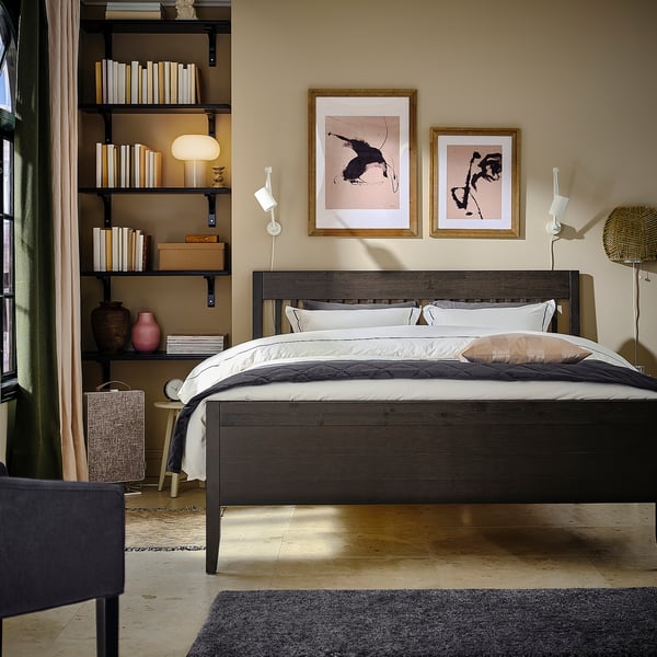 Modern bedroom with IDANÄS dark brown wooden bed, white linens, abstract wall art, and black bookshelf with decor.