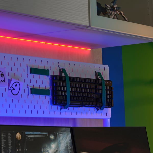 Wall-mounted pegboard with keyboard, stickers, & colourful led lights. Small action figure on shelf.