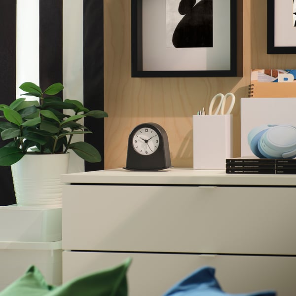 Modern workspace with KÄRRSÅNGARE alarm clock, plant, pink pencil holder on white desk.