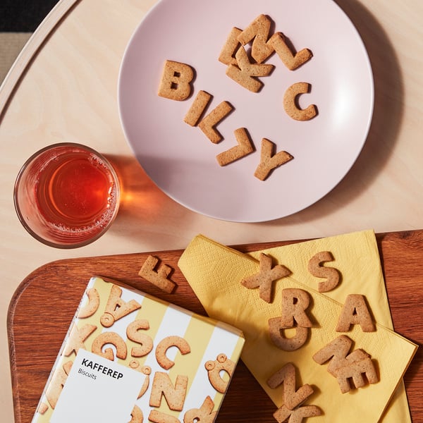 Alphabet cookies spell billy on pink plate, with yellow box and drink on wood table.