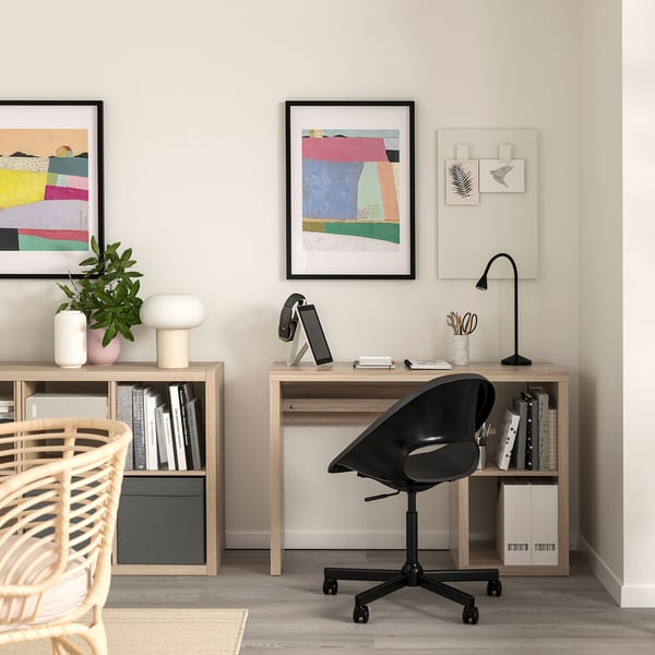 Home office with wooden desk, black swivel chair, and bookshelves, adorned with colourful art and neat decor.