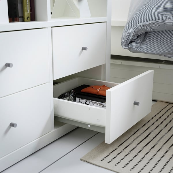 Open white dresser with an orange folder and black and white booklet inside. Part of KALLAX storage solution.