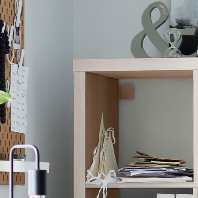 Wooden KALLAX shelf with notes, items, and a plant.